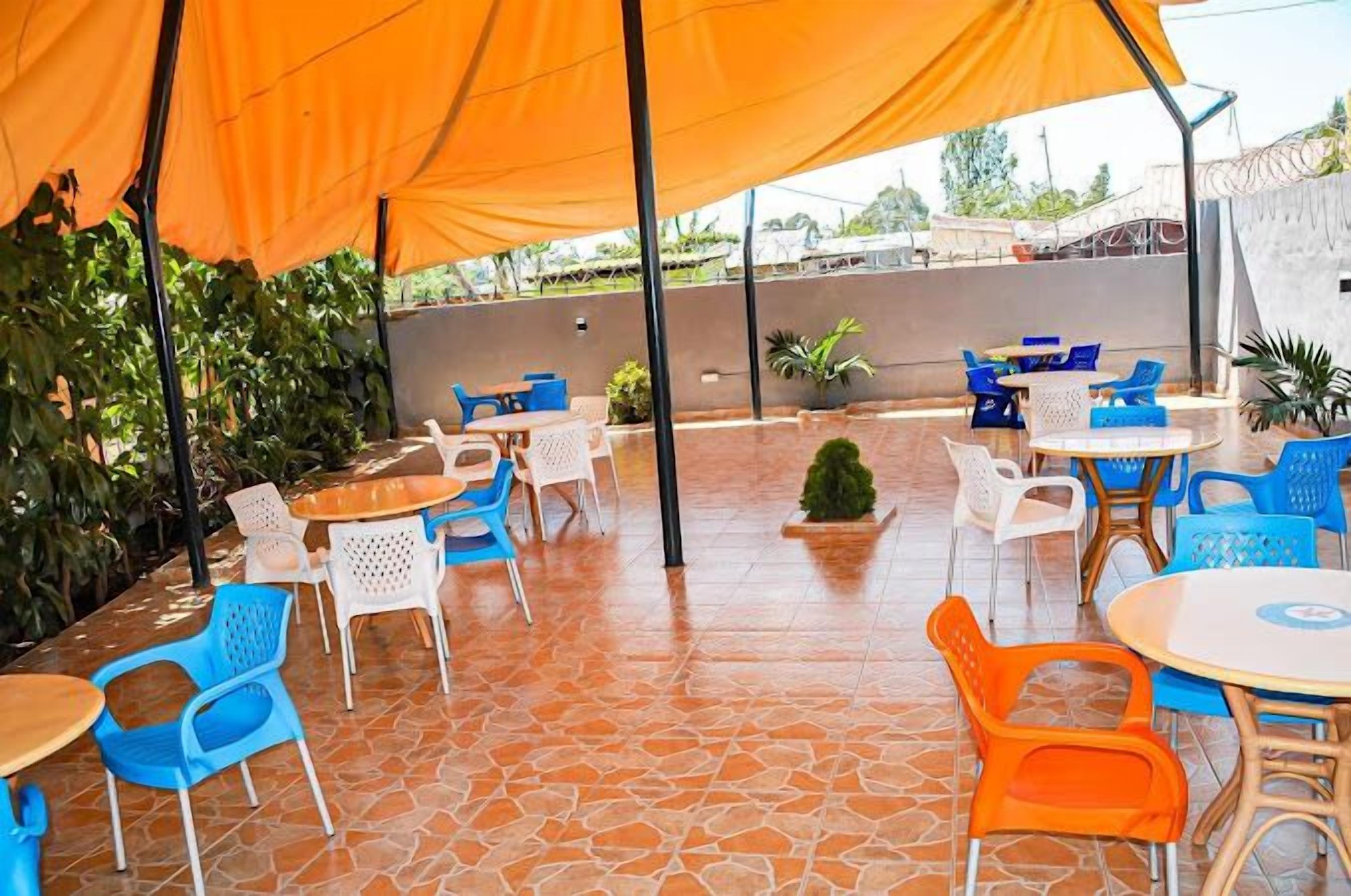 An outdoor patio area with orange canopies, blue and white plastic chairs, and terracotta-tiled flooring.
