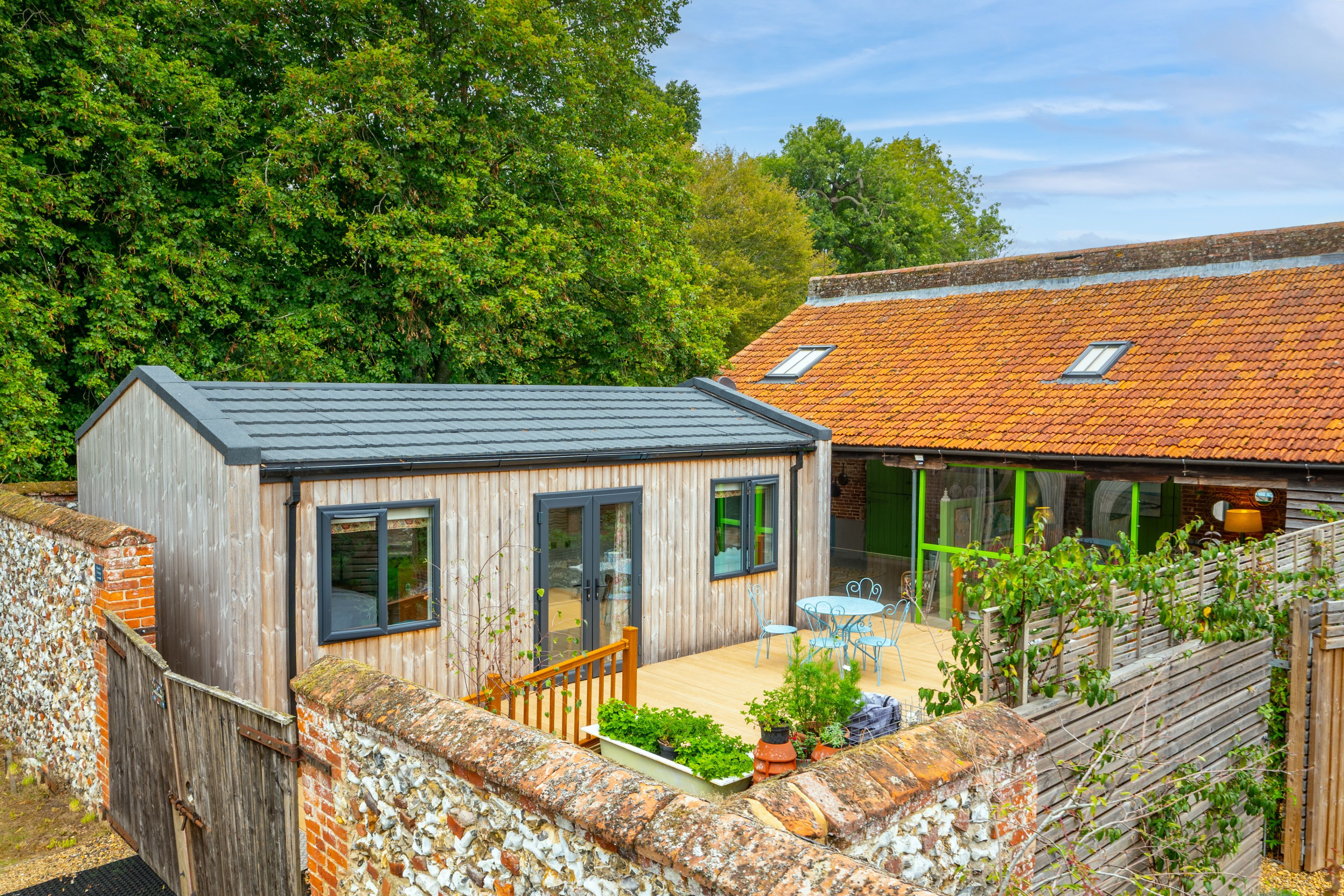 A small wooden house with a sloped roof, a patio with outdoor furniture, and a garden area with plants.