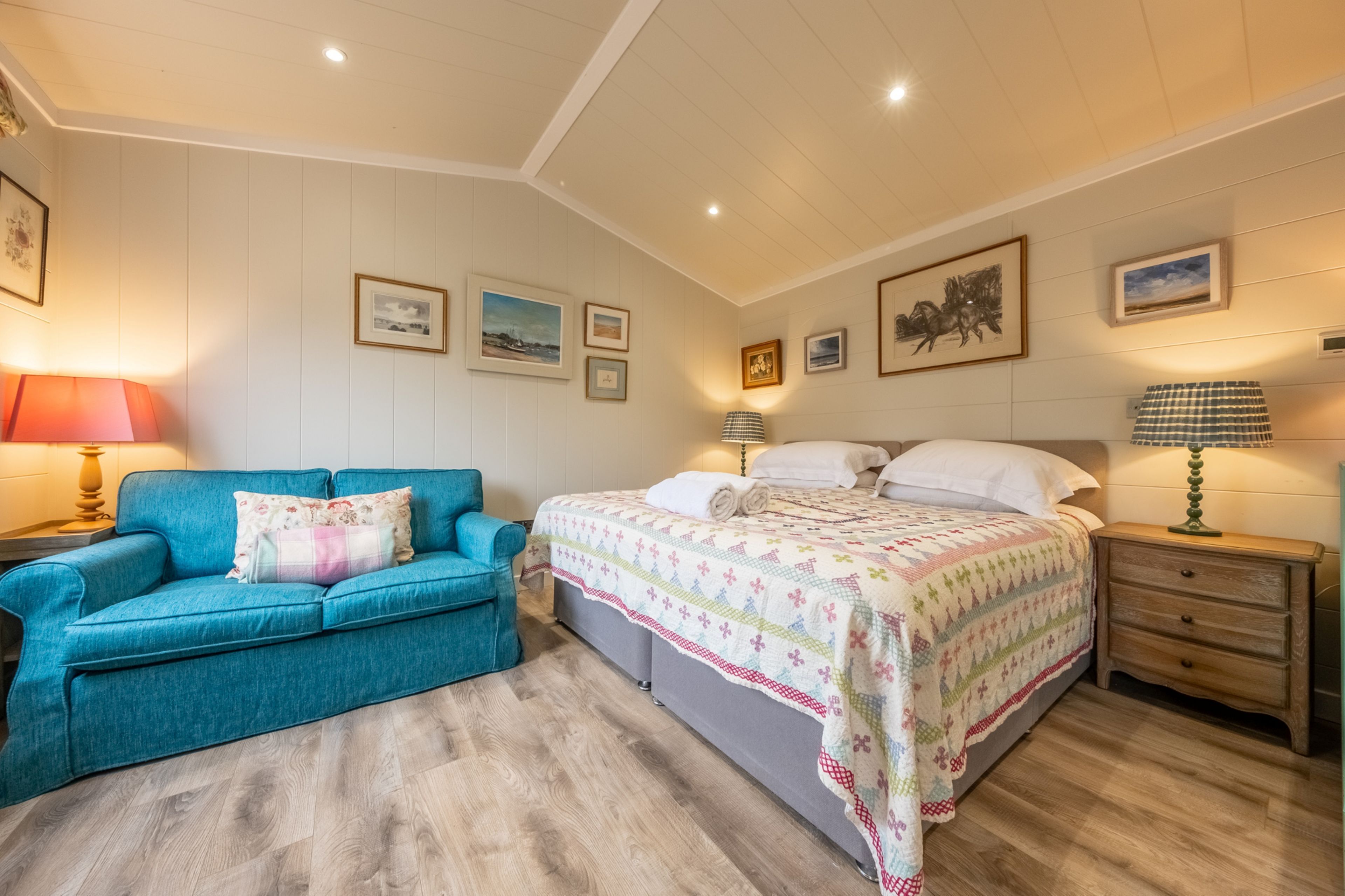 A bedroom with a bed, a blue sofa, a wooden nightstand, and wall-mounted lamps.