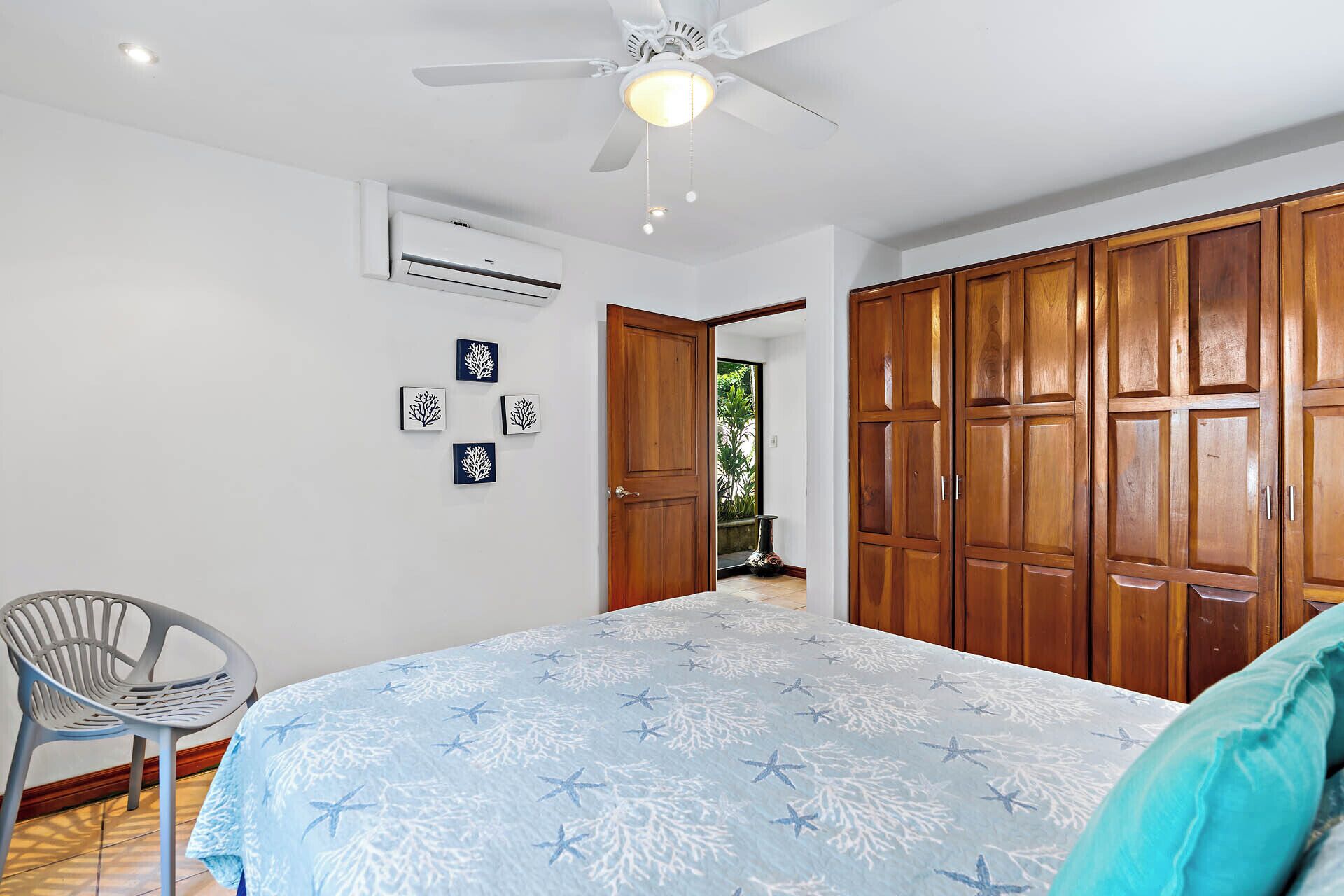 Un dormitorio con cama, ventilador de techo, equipo de aire acondicionado, armarios de madera y una silla.
