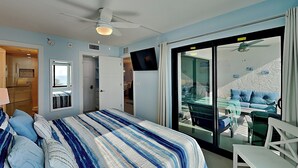 A bedroom with a bed, a TV, a ceiling fan, and a balcony with a table and chairs. - Seaside 407 | Balcony, Pool, Grill Area + Direct Beach Access (Fort Myers Beach)