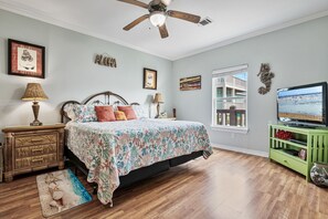 A bedroom with a bed, a ceiling fan, a television, and a window with a view of a balcony. - Outlaw's Inn - Gulf View, fenced yard, outdoor bar - 3 Bedroom (Crystal Beach)