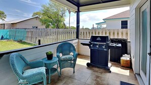 Eine überdachte Terrasse mit zwei Korbstühlen, einem kleinen Tisch mit einer Pflanze und einem Grill.