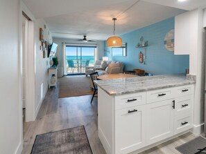 A modern kitchen with white cabinetry, a large island, and a view to the outside.