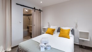 A modern hotel room with a bed, two bedside tables, a shower, and a toilet.