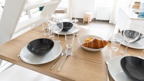 A breakfast table set with plates, bowls, cutlery, glasses, and a croissant.