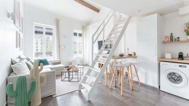 A modern living space with a staircase, a sofa, a dining area, and a washing machine.