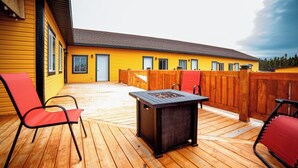 A wooden deck with a fire pit, red chairs, and a yellow building in the background. - HOTELLERIE PUAMUN (Aguanish)