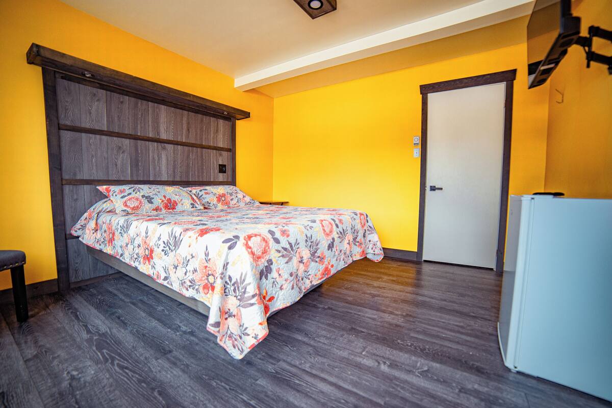 Un dormitorio con cabecera de madera, colcha estampada con motivos florales, un banco y una puerta.