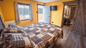 A bedroom with a large bed, a TV mounted on the wall, and a sliding door leading to a bathroom. - HOTELLERIE PUAMUN (Aguanish)