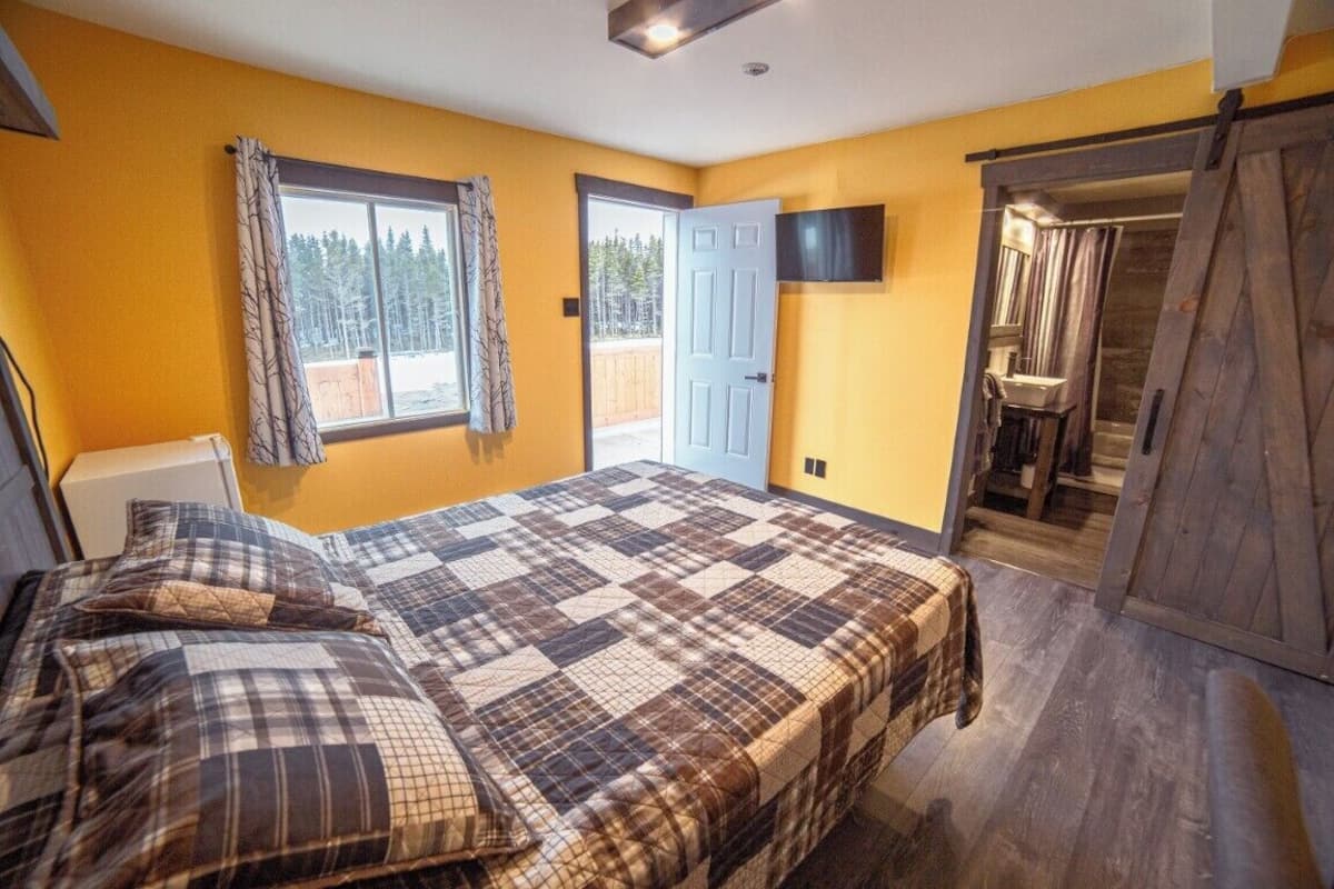 Un dormitorio con una cama grande, un televisor montado en la pared y una puerta corredera que da al baño.