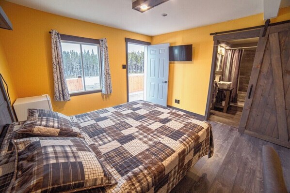Una camera da letto con un letto grande, una TV montata a parete e una porta scorrevole che dà su un bagno.