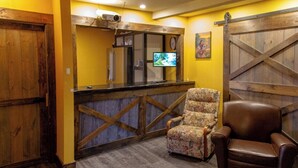 A room with a wooden door, a counter with a television, a floral armchair, and a brown leather chair. - HOTELLERIE PUAMUN (Aguanish)