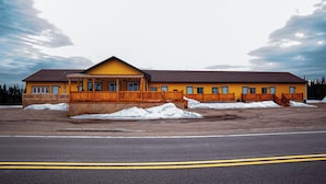 A yellow building with a wooden deck and a large parking lot. - HOTELLERIE PUAMUN (Aguanish)