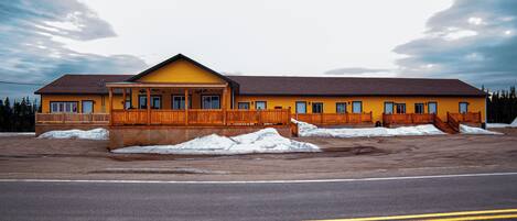 A yellow building with a wooden deck and a large parking lot.