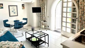 A living room with a dining table, chairs, a coffee table, a TV, and a large window with curtains.