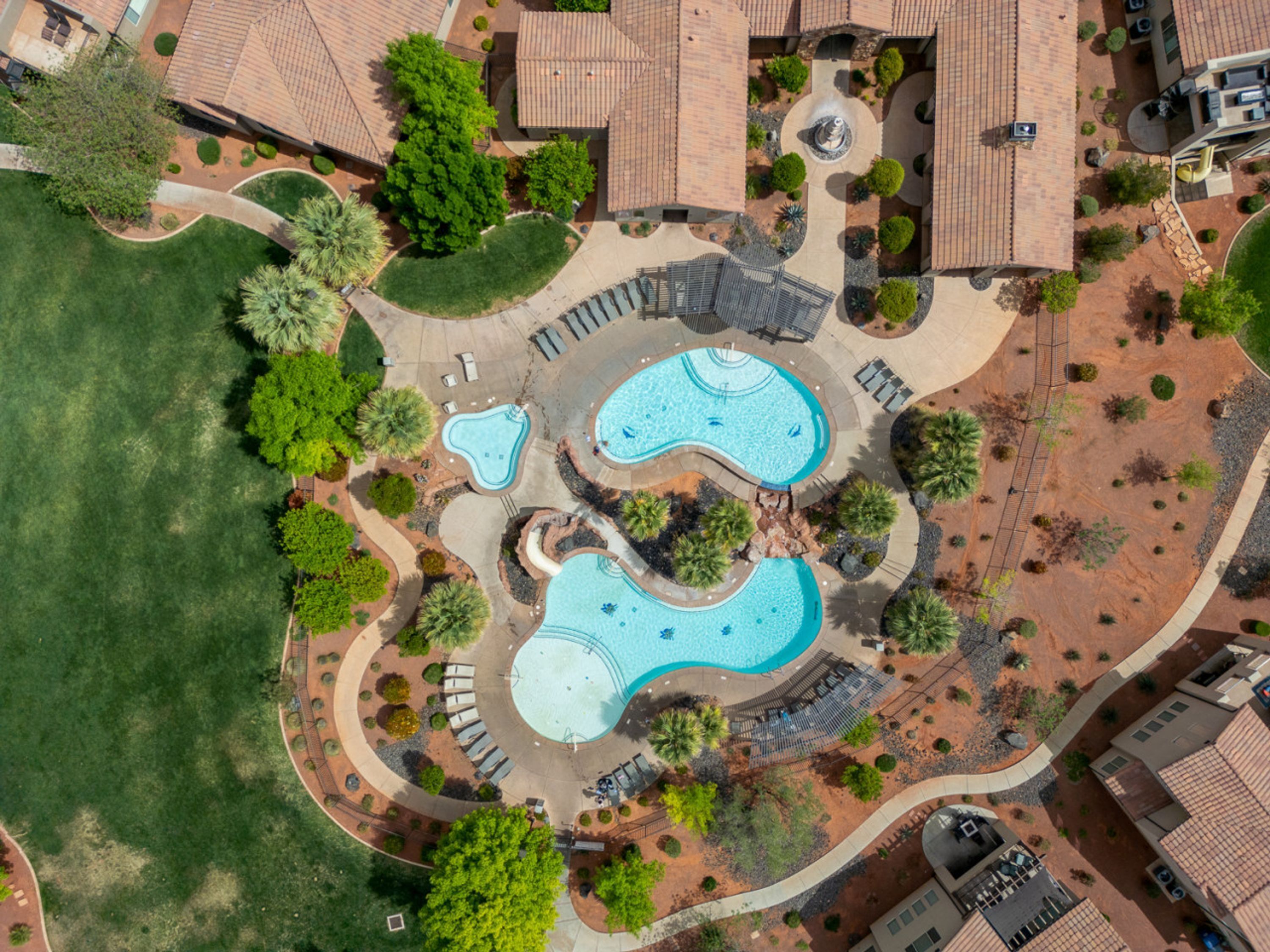 Vue aérienne d’un quartier résidentiel avec deux piscines, entouré de jardins aménagés et de quelques maisons.