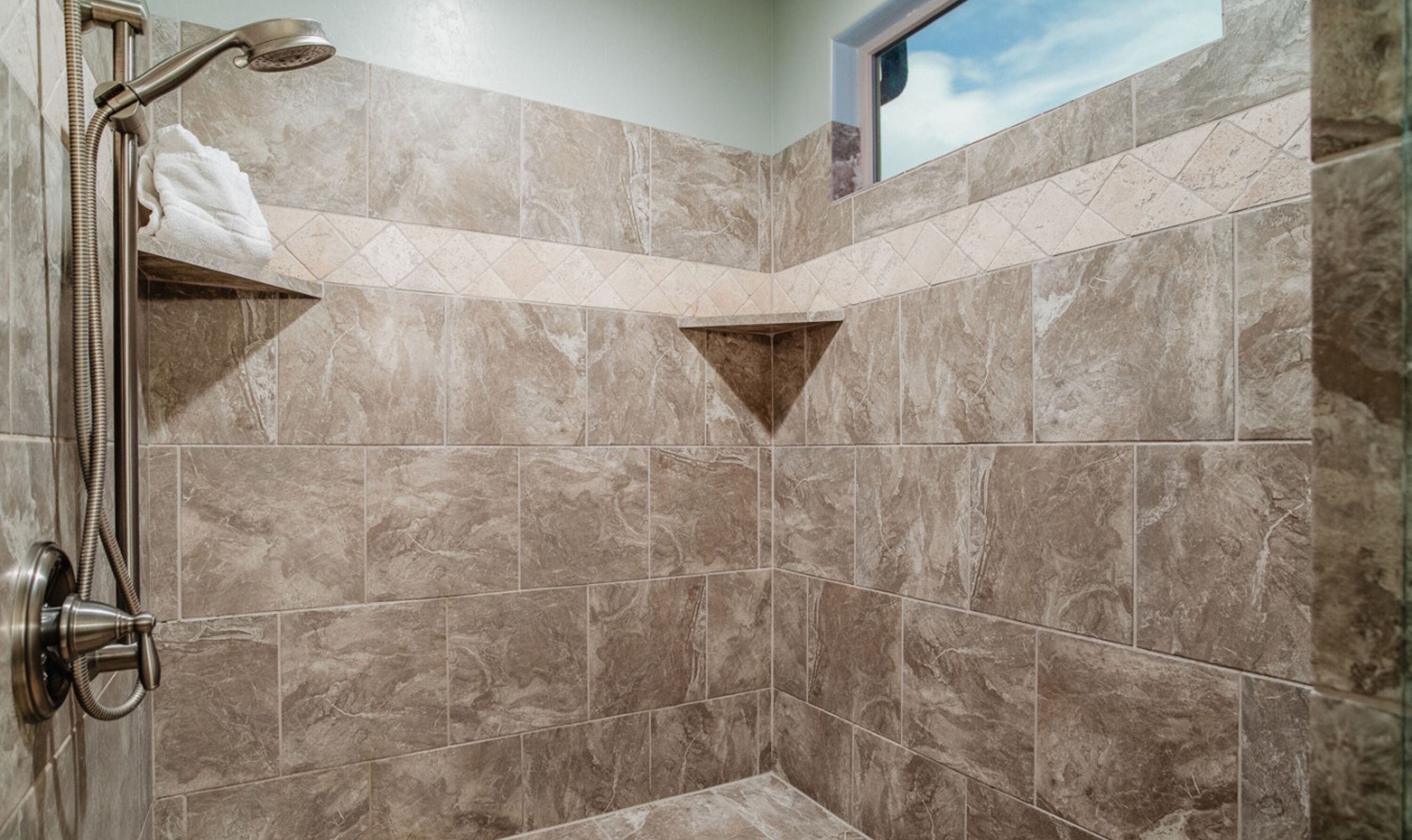 A shower area with a handheld showerhead, a towel rack, and a window with a view of the sky.