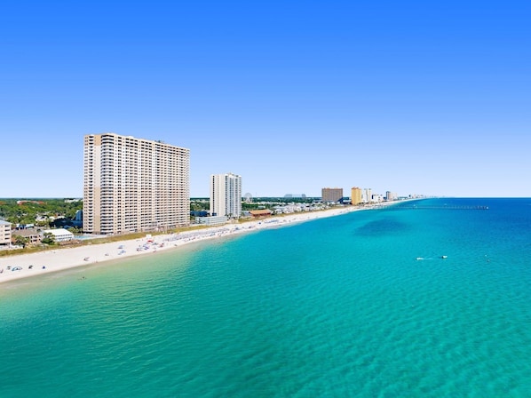 Eine Küstenlandschaft mit einem Strandhotel, klarem türkisblauem Wasser und wolkenlosem Himmel.