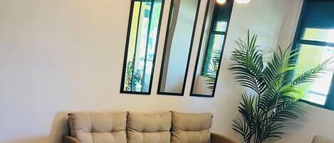 A cozy living room with a sectional sofa, a coffee table, and wicker furniture. There are three wall mirrors and a potted plant.