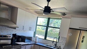 Cozinha moderna com armários brancos, geladeira de aço inoxidável, forno embutido e uma janela que proporciona luz natural.