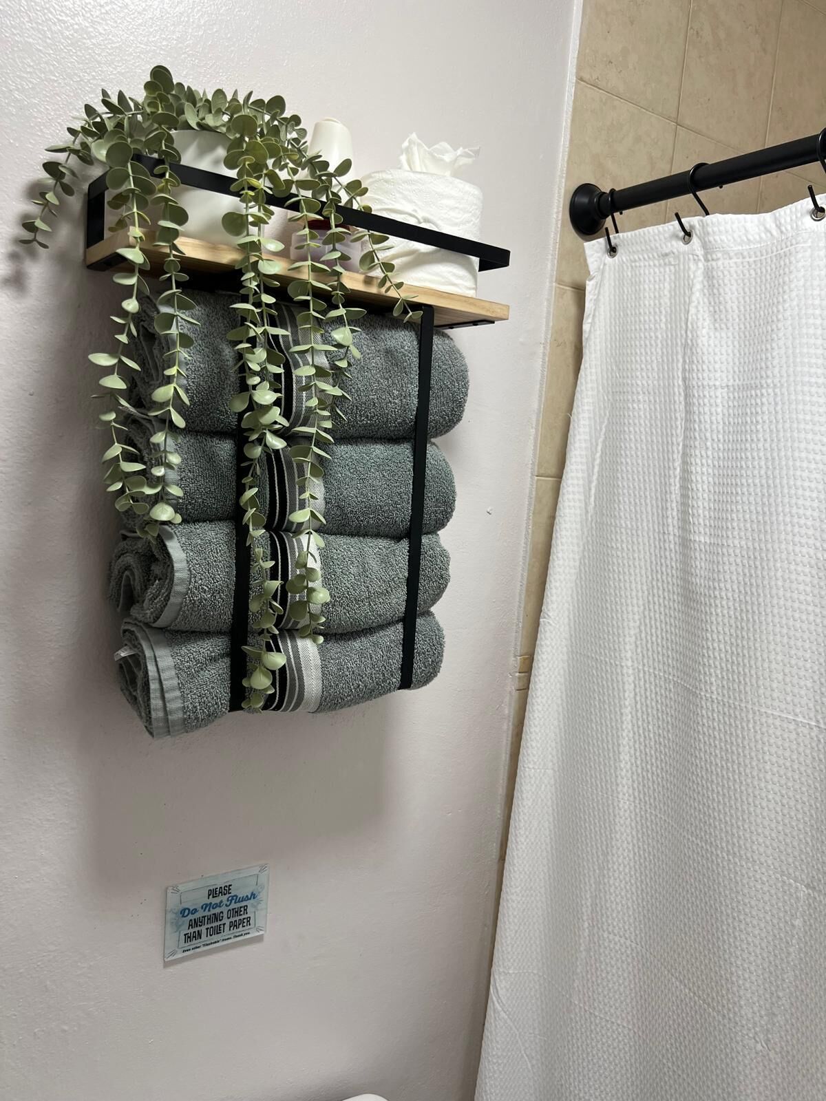 A bathroom with a towel rack holding multiple towels and a sign instructing not to flush anything other than toilet paper.