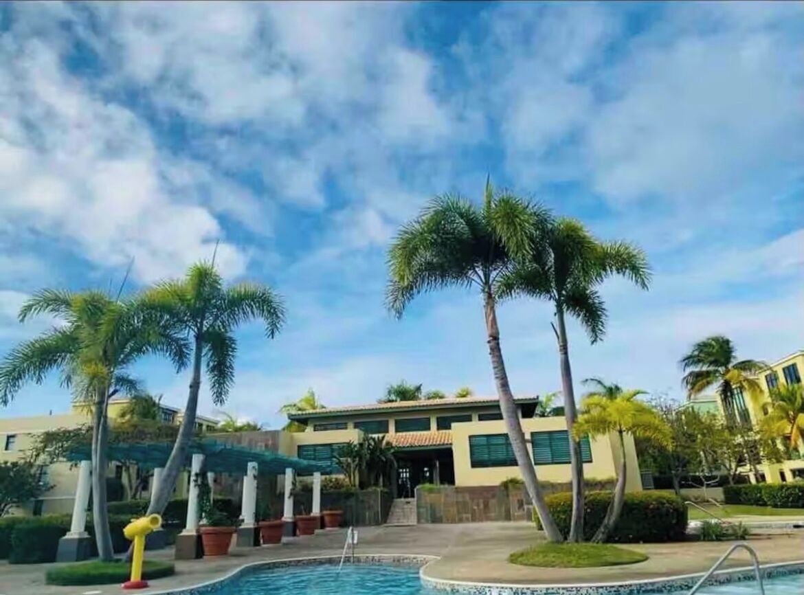 Et hotel med pool, palmer og en klar himmel.