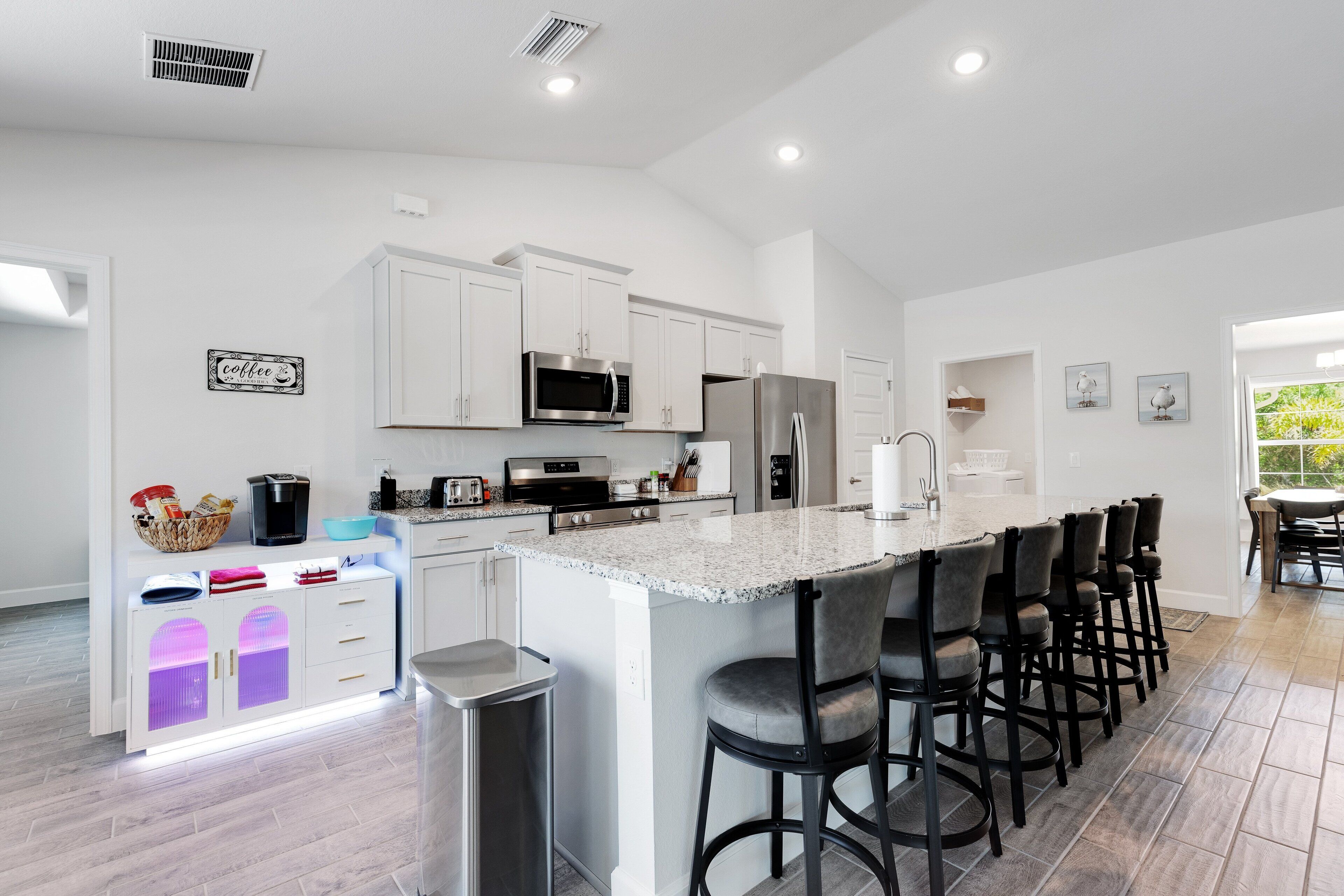 A modern kitchen with white cabinets, a central island with bar stools, stainless steel appliances, and a bright, airy design.