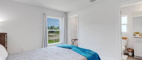 A bedroom with a bed, a window, a door leading to a bathroom, and a view of the outdoors.