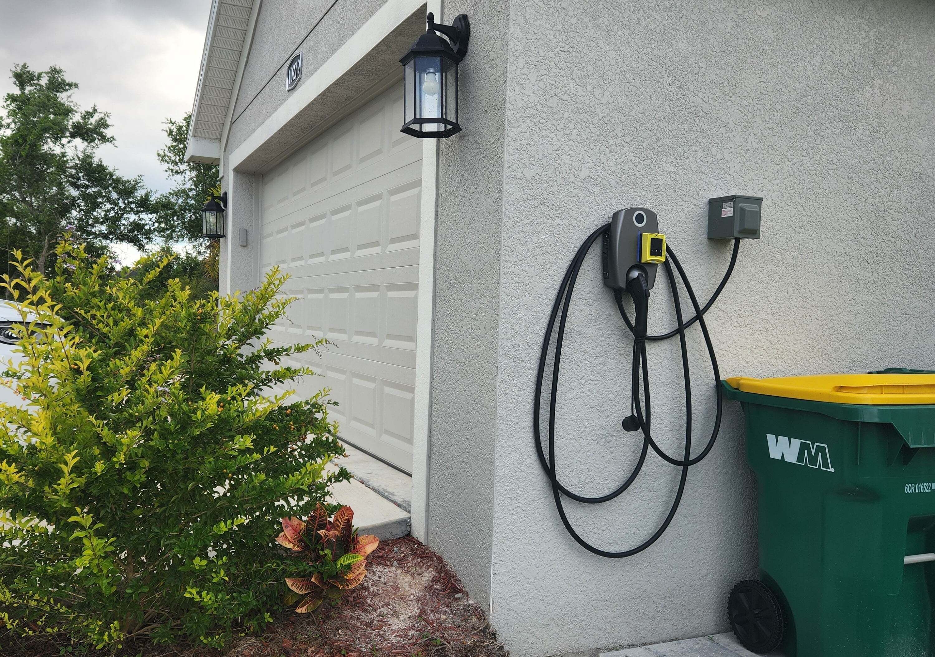 A garage door, a wall-mounted light fixture, and a green recycling bin.
