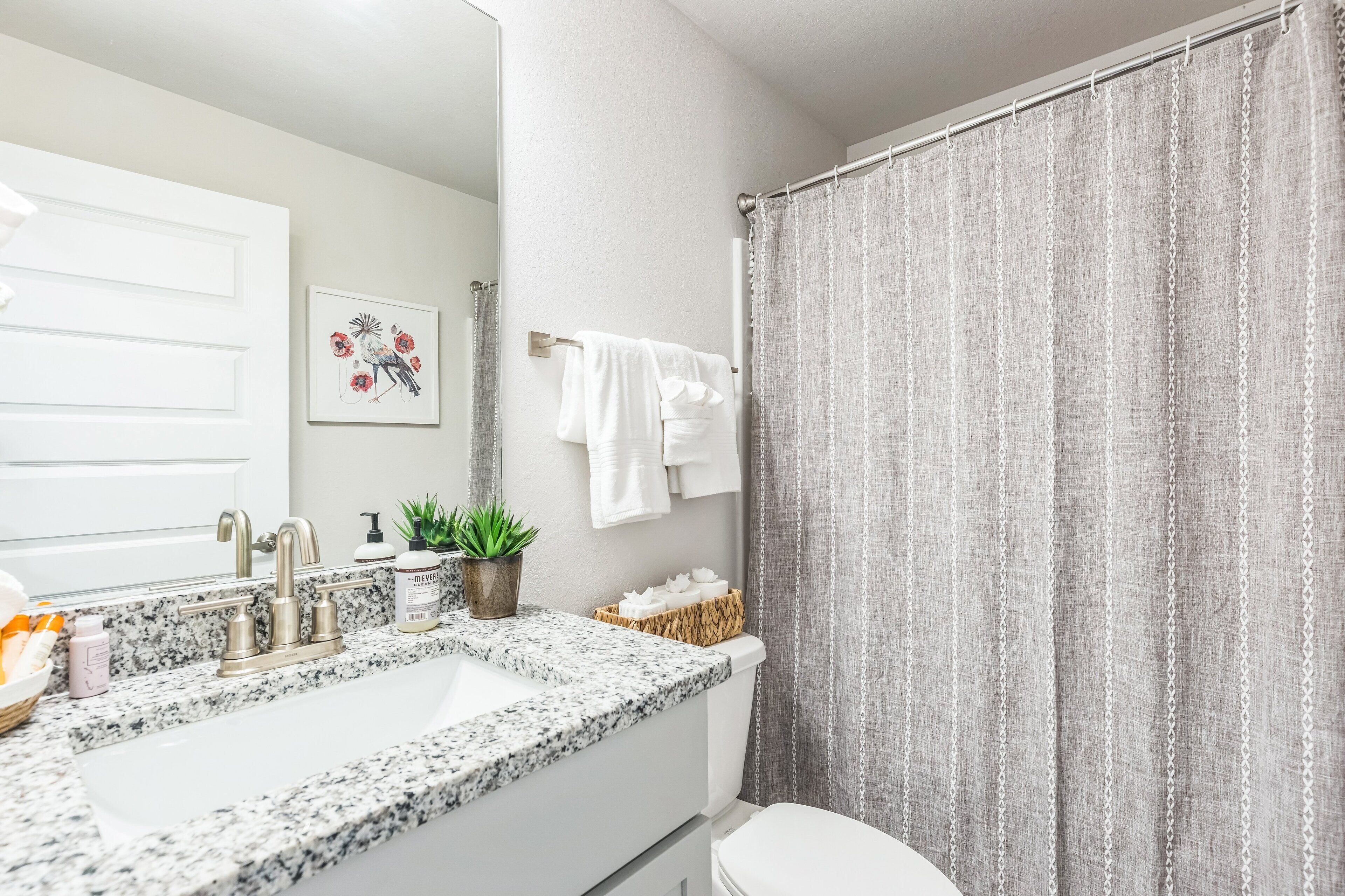 A bathroom with a granite countertop sink, a white toilet, a shower curtain, and a wall-mounted towel rack.