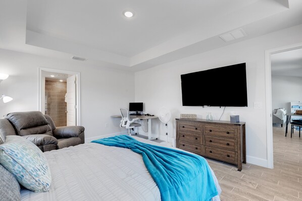 A modern bedroom with a bed, a desk, a chair, a dresser, and a TV mounted on the wall. - New Poolside Home in South Gulf Cove! Beaches Boca Grande, Manasota, Siesta Key & Venice (Port Charlotte)