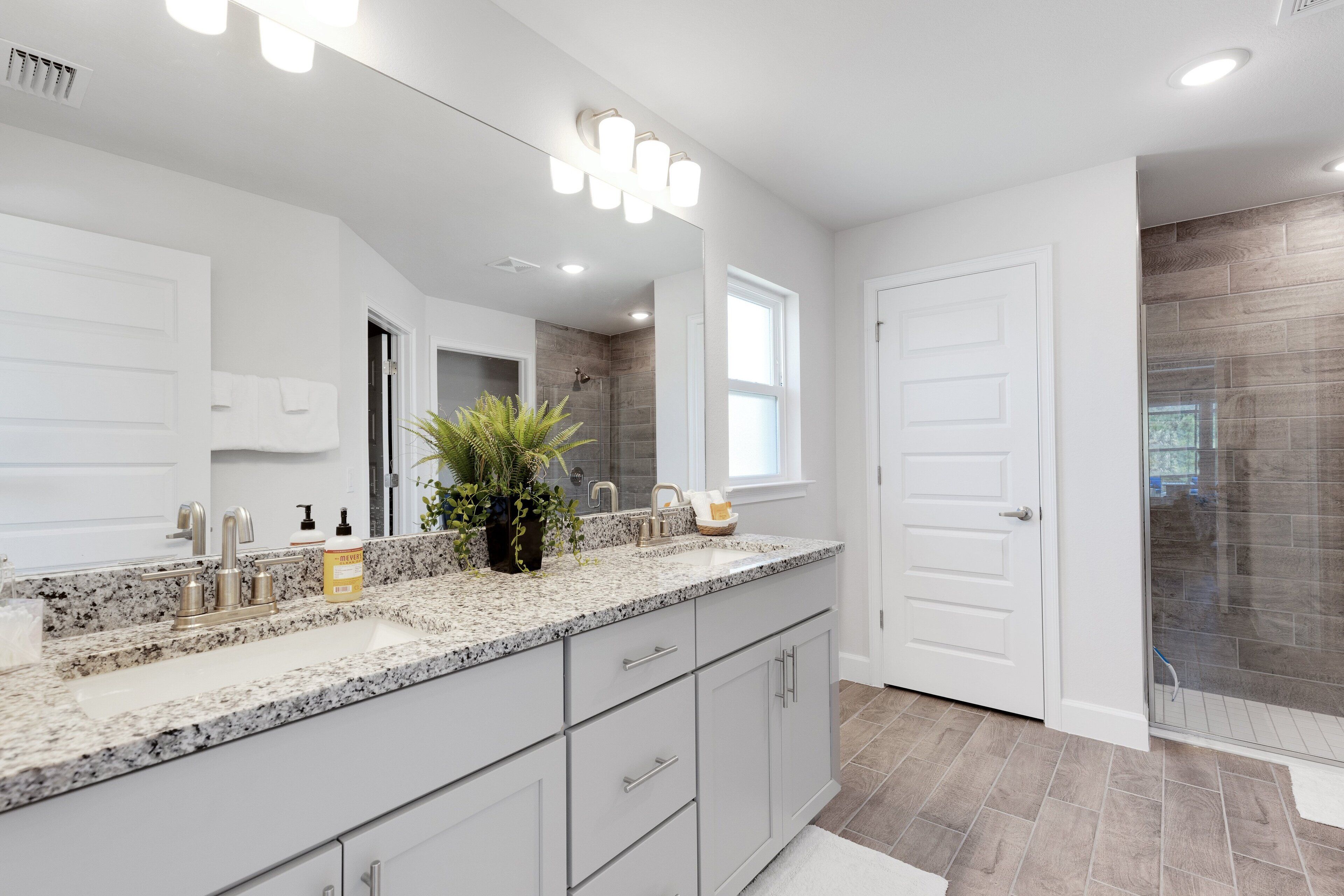 A modern bathroom with a large vanity, a shower with a glass door, and a large mirror with lights.