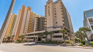 A multi-story hotel with a central parking structure, surrounded by palm trees and other greenery. - Stunning Ocean Views From The 10th Floor 1 Bedroom Condo (North Myrtle Beach)