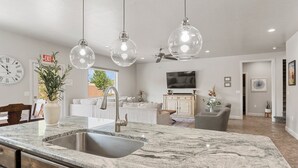 Eine moderne Küche mit Marmorarbeitsplatte, Edelstahlspüle und Pendelleuchten.