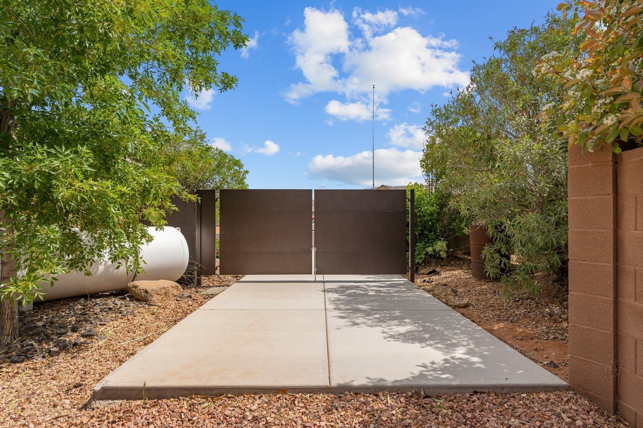 A concrete patio with a metal gate, surrounded by trees and a brick wall.