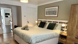 A bedroom with a bed, bedside tables, a wardrobe, a painting on the wall, and a door leading to another room.