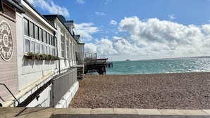 A building with a sign that reads "Coffee & Tea" next to a pebbled beach with a pier extending into the water.
