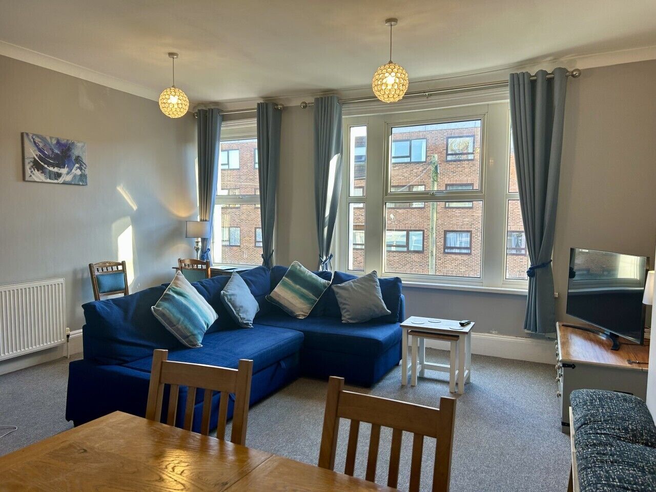 Ein Wohnzimmer mit blauem Sofa, einem Esstisch und einem Fernseher.