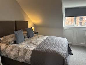 A bedroom with a bed, pillows, a nightstand, a window, and a door.