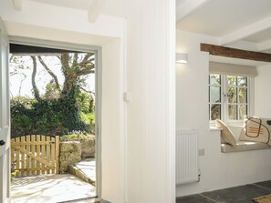 A white interior with a wooden door leading to a garden, a window with a view of greenery, and a radiator on the wall. - Sunrise Cottage (Bodmin)