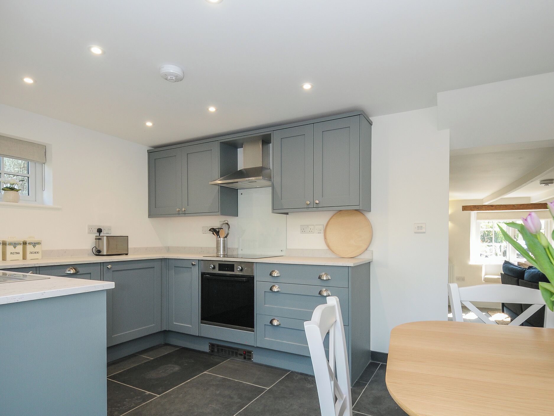A modern kitchen with grey cabinets, a built-in oven, and a round wooden cutting board on the countertop.