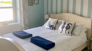 Una cama bien hecha con ropa de cama blanca y azul, un candelabro y paredes a rayas.