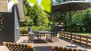 An outdoor deck with a table and chairs, a wooden fence, and a large umbrella. - Stunning home in Oksbøl with sauna (Oksbøl)