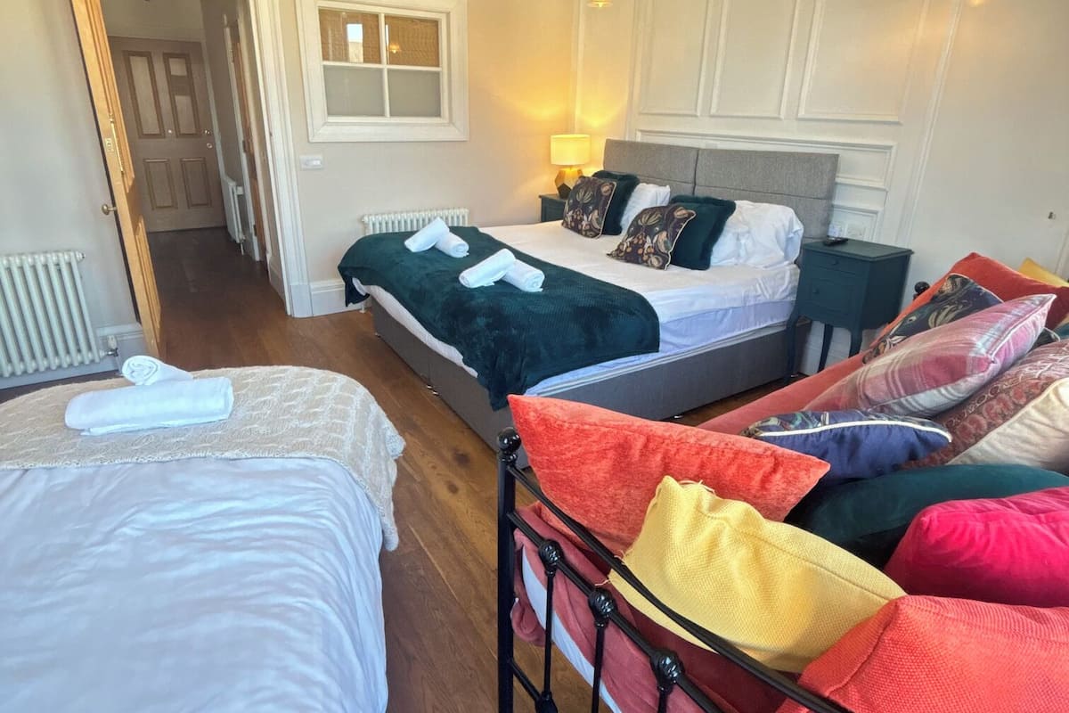 Ein Hotelzimmer mit zwei Betten, einer Sitzecke mit bunten Kissen, einem Heizkörper und einem Fenster mit Milchglas.