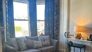 A cozy living room with a grey sofa, patterned curtains, a wooden floor, and a table with a lamp and decorative items. - No. 1 High Street - Boutique Rooms (Markinch)