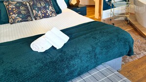 A neatly made bed with a teal blanket and pillows, a bedside table with a lamp, and a view of a bathroom with a bathtub and a towel rack. - No. 1 High Street - Boutique Rooms (Markinch)