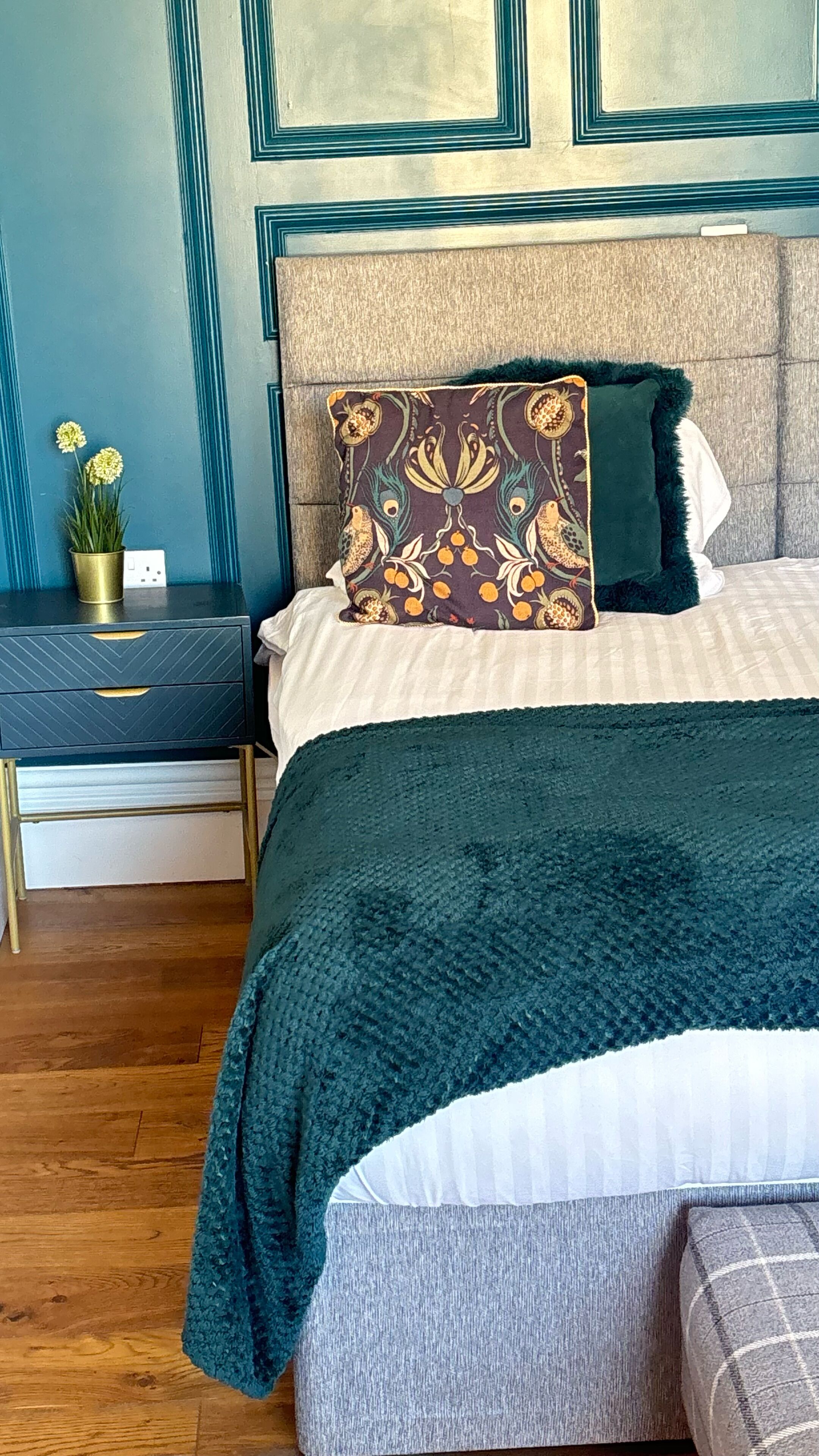 A bedroom with a bed, a nightstand, a potted plant, and a wall with decorative molding.