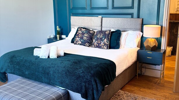 A bedroom with a large bed, a bench, a nightstand, and a lamp. - No. 1 High Street - Boutique Rooms (Markinch)