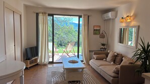 A living room with a sofa, a coffee table, a TV, and a view of a garden through a sliding door. - (New) Superb apartment in Golf (Saumane-de-Vaucluse)
